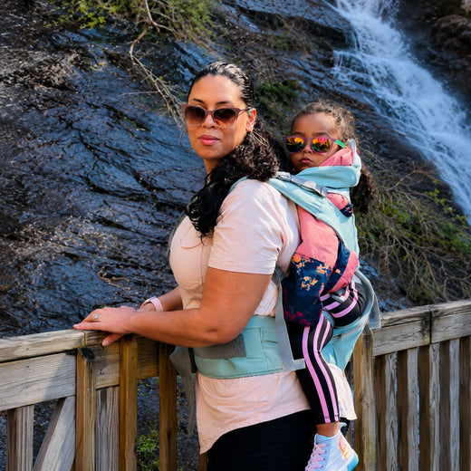 A mom carrying her toddler on her back in Grow+ by a waterfall